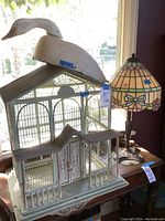 Full view of bird cage, paper mâché duck and stained glass lamp on table