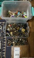 Large translucent plastic container partially filled with vintage buttons, floral embellishments, and button accessories in multiple colors and materials.