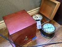 Closed dark wood box next to open wood box and two brass clocks on floor