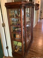 Front and side view of the wooden curio cabinet, showing the glass doors and shelves inside with various decorative items.
