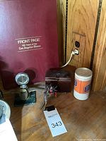 The full lot including Boyce Moto Meter, LA Times book, small brown leather box, plastic drink container, and metal bird decor arranged on wooden surface.