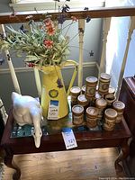 Wide view showing yellow metal jug with floral decoration, white goose statue, and collection of Edison Gold Moulded Records tubes arranged on a wooden table.