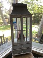 Full view of the cabinet showing closed glass doors and two drawers below, with the birdhouse inside.