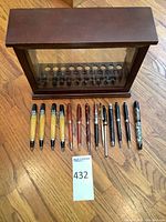 All 13 pens arranged in front of wooden and glass display case