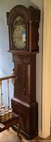 Full height view of dark wood tall-case clock showing hood, trunk and base