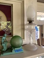 Clear glass hurricane and green figural lamp shown side by side on shelf