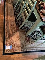 Overall view of rectangular floral needlepoint rug under table and chairs on hardwood floor