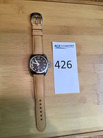 Full view of watch front showing brown dial, tan leather strap and ACP lot number card