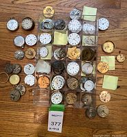 Overview of clear plastic grid containing pocket watch dials, movements and loose parts on wooden floor