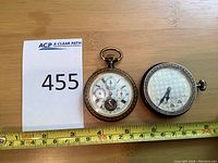 Two watches side by side with measuring tape and lot number card visible