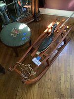Photo showing wooden sled with wooden duck figure on top and small stool with embroidered seat next to it on wood floor.