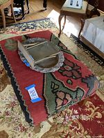 Photo of the Southwestern wool ottoman with southwest pattern in red, green, black, and beige colors, with a decorative metal tray and picture frame on top.