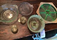 Top-down view of all lot items on wooden tabletop: green mixing bowl, clear plates, hobnail bowl, candlestick holders, sectioned tray