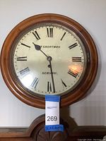 Front view of the wooden wall clock showing the Roman numeral dial with the brand name 'Shortman' and 'Newham'. Clock is mounted on a wall with 16 x 6 inch measurements labeled.