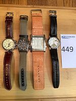 Four watches laid flat on wood board showing dials and straps