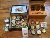 Open Belicoso wooden cigar box filled with assorted watch case housings, dials, movement parts and separate wooden stand with metal punch dies