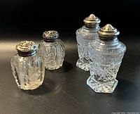 Four vintage salt and pepper shakers with clear cut glass bodies and silver tops, two distinct design pairs shown.