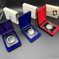 Three Canadian nickel dollar coins from 1970, 1973, 1976 in blue, blue, and red velvet-lined clamshell boxes with outer protective covers.