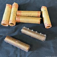 Seven rolls of Canadian pennies on black background, some labeled with years 1975, 1977, 1978, 2000, and conditions AU, RBC.