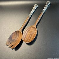 Pair of wooden salad servers with silver handles shown flat on a black background.