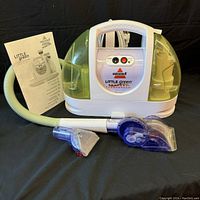 Full front view of Bissell Little Green compact deep cleaner showing hose, two attachments, and instruction manual.