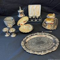Overview of complete lot on black cloth showing all silver plate items including trays, egg cups, spoons, and serving pieces
