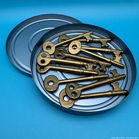 Photo showing several brass-colored skeleton keys inside an open metal film reel tin on a blue background.