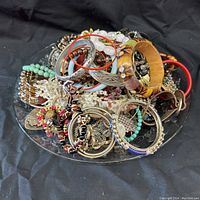 Wide view of assorted costume jewelry including bangles, bracelets, necklaces, and pins laid on a dish.