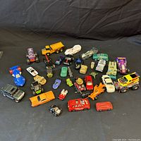Photo showing about 33 assorted toy vehicles including cars, trucks, planes, and other vehicles spread out on a black background.