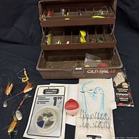 Opened brown Old Pal 1058 fishing tackle box showing tiered compartments with a variety of fishing lures inside and fishing accessories laid out in front.