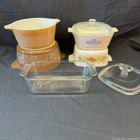 Group photo showing all dishes including round brown Corningware with floral pattern, square Corningware with blue cornflower and vegetable patterns, and clear Pyrex rectangular dish with lid.