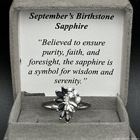 Ring inside grey velvet box with informational card about sapphire birthstone.