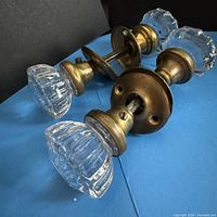 Two sets of vintage glass door knobs with brass mounting hardware on blue background