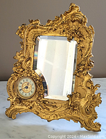 Front view showing the ornate gold-tone Rococo style frame with built-in beveled mirror and the clock inset on the left side.