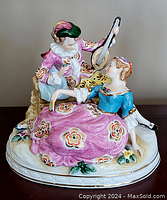 Front view of the porcelain figural group depicting the musician with lute and a lady seated, showing colorful detailed clothing and floral base.