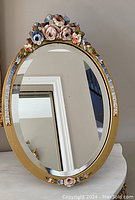 Front view of oval antique mirror showing floral wood frame and mirror surface with reflections.