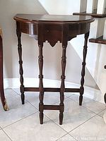 Front view of antique semi-circular side table showing turned legs and minor surface wear
