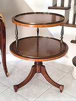 Full view of antique two-tiered round wooden table with three curved legs and brass detailing.