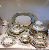 Overview of the entire Aynsley dessert set including stacked dinner plates, dessert plates, saucers, cups, and one large serving platter, all with blue and gold leaf decorative edging.