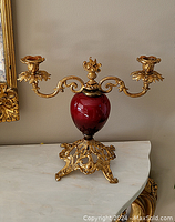 Full view of double-arm candle holder with red ceramic body and gold decorative metal parts.