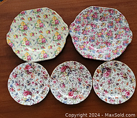Top view of all five chintz plates showing intricate multi-colored floral patterns and scalloped edges with gold trim.