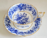 Blue and white floral patterned cup resting inside matching saucer, both featuring gold trim on rims and handle, shown from an angle.