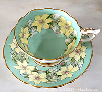 Top view of cup and saucer showing yellow flower wreath design and gold trim.