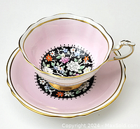 Pink porcelain cup and saucer with scalloped edges, floral pattern in center, and gold trim.