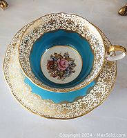 Top-down view of the cup stacked inside the saucer showing gold fleur-de-lis pattern and floral centerpiece inside the cup.