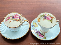Two EB Foley floral teacups and saucers side by side on a wooden surface, showing the different floral patterns and gold accents.