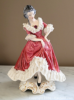 Front view showing full figure with pink dress and white lace, seated pose, and ornate base