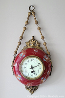 Front view of the French red hand-painted floral clock with gold-tone metal decorative accents and hanging chain.