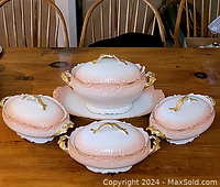 Top down photo showing all four pink and white Limoges tureens with gold handles on a wooden table.