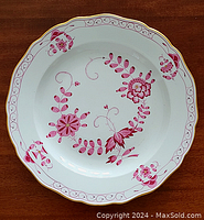 Full view of white porcelain plate with pink floral designs and gold trim with scalloped edge